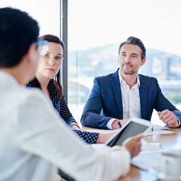 Three professionals engaged in a business meeting around a table with a tablet.