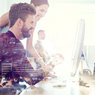 Two colleagues smiling and working together at a computer in a bright office.