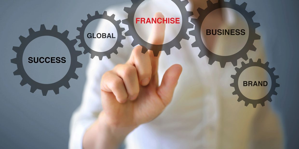 Hand pointing to the word 'FRANCHISE' among business-related gears.