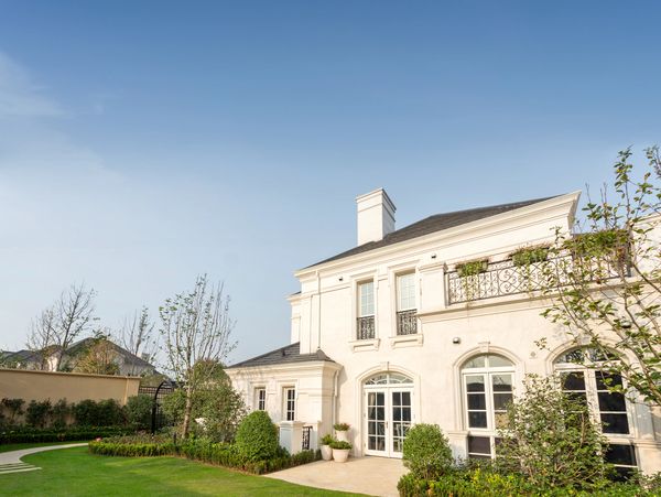Elegant white two-story house with a manicured garden under a clear blue sky.