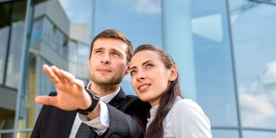Two business professionals looking and pointing ahead outside a modern glass building.
