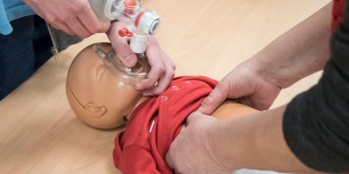 Hands performing CPR on a baby mannequin.