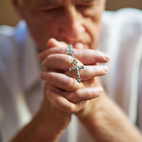 A person holding a rosary with a cross, eyes closed in prayer.