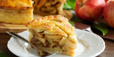 A slice of apple pie on a white plate with a fork.