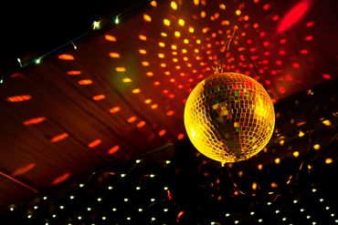 A glowing disco ball casting vibrant red and yellow reflections on a dark ceiling.