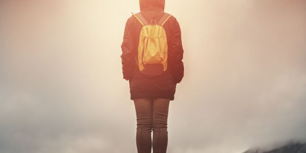 Person with yellow backpack stands contemplatively in foggy landscape.