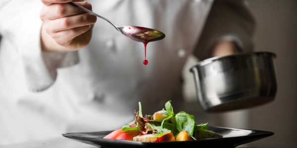Chef delicately drizzling sauce over a fresh salad on a black plate.