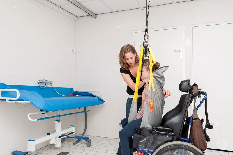 Disability a disabled child being lifted out of a wheelchair using a special needs lift being operated by a carer. Image shows people working with physically and mentally handicapped people