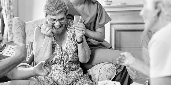 Elderly people and a caregiver joyfully playing cards together.
