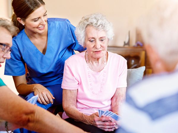 Elderly woman playing cards with a nurse and friends.