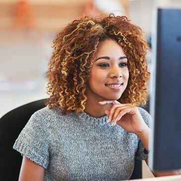 Image of a young lady working at a computer. She is smiling.