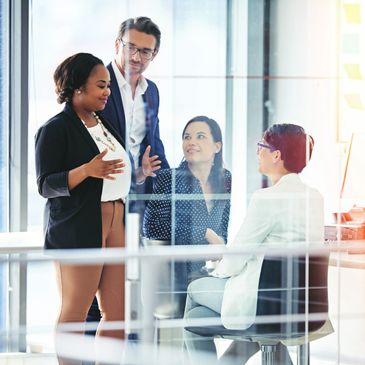 Four professionals engaged in a discussion inside a modern office space.