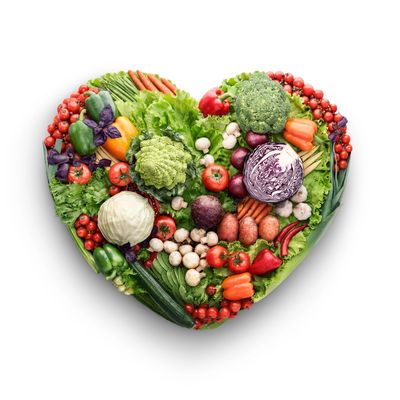 Heart-shaped arrangement of fresh colorful vegetables on white background.
