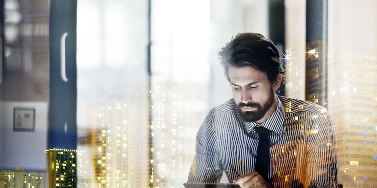 A man in a striped shirt working intently with city lights reflected around him.