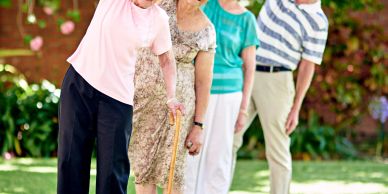 Four elderly people exercising outdoors in a garden.