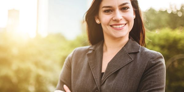 Confident woman smiling outdoors in professional attire.