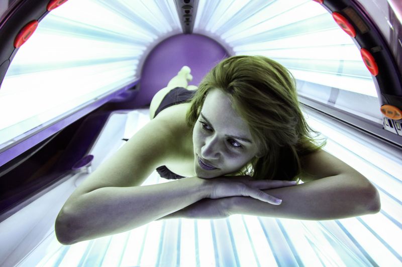 Young beautiful woman lying on a tanning bed in a solarium. About 25 years old, Caucasian female in black bikini.