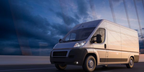 White delivery van driving on empty road at dusk.
