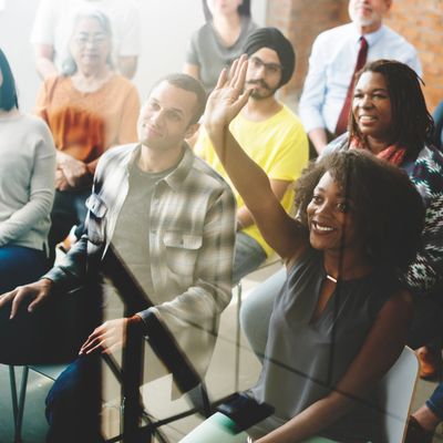 Diverse group in a seminar with a woman raising her hand to participate.