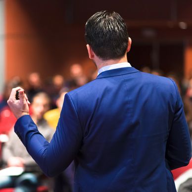 Man in blue suit giving a presentation to an audience.