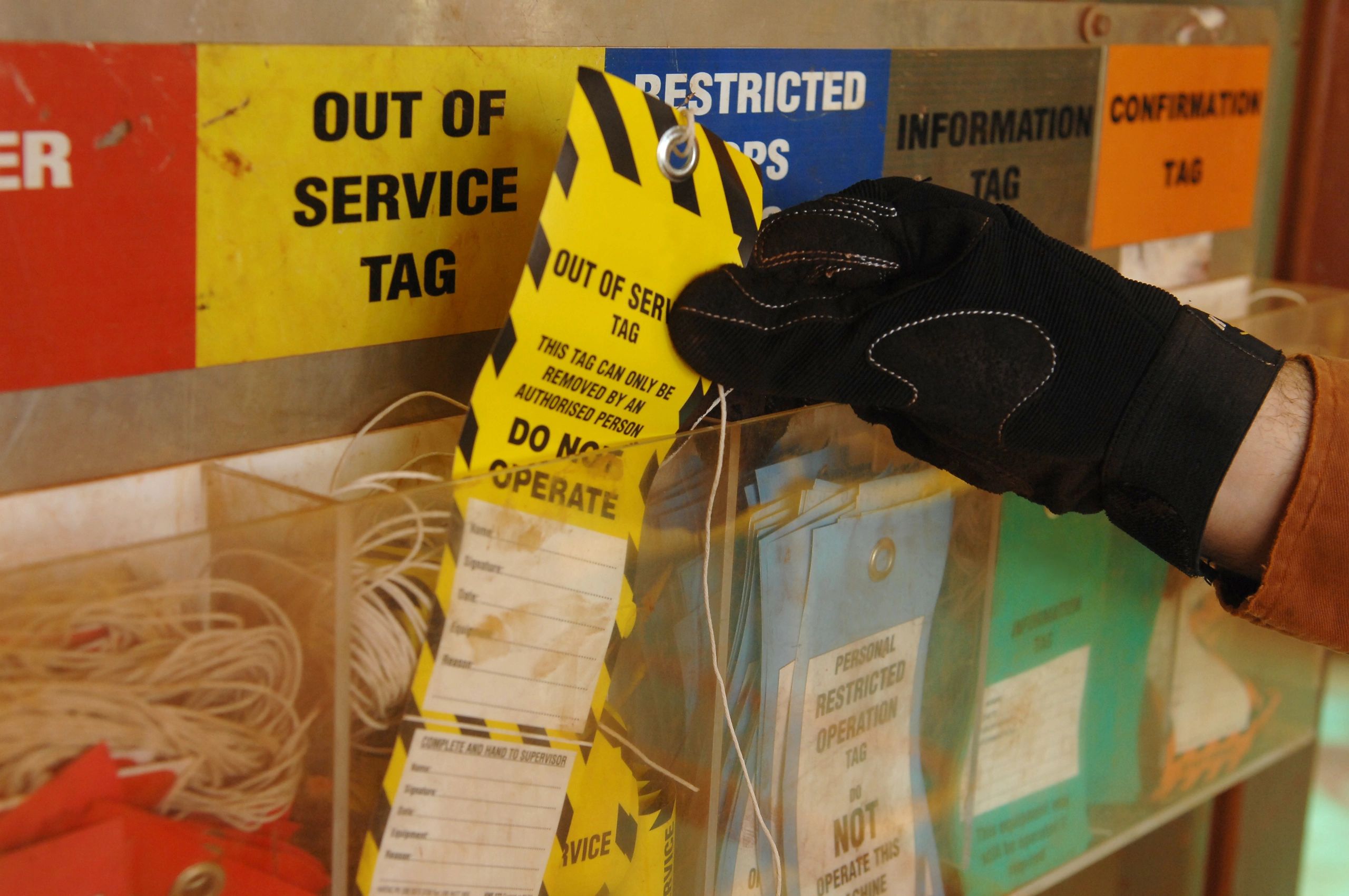 Gloved hand placing a Do Not Operate lockout tag on equipment