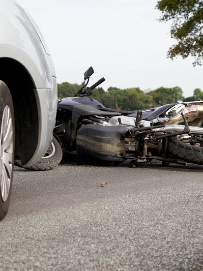 A gray car hit a turned over motorcycle.