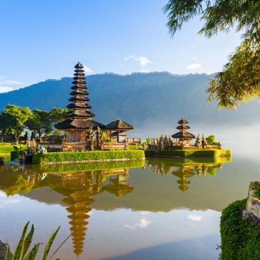 Scenic view of a traditional Balinese temple by a lake with mountain backdrop.