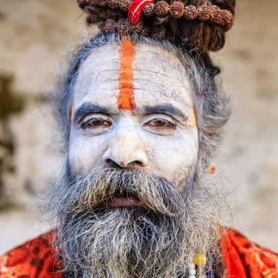 Portrait of a man with ash-covered face and red tilak mark.