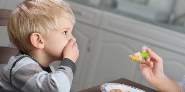 A young boy refuses to eat while being fed by an adult. Autism nutrition guide, dietary strategies for autism, gut health support, picky eating solutions.
