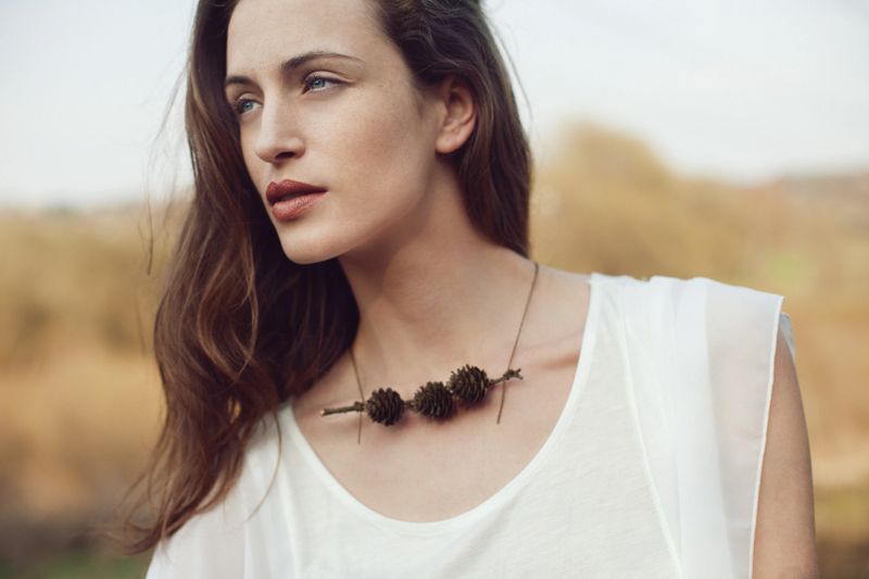 Portrait of confident young woman in nature. She is natural beauty, no skin filtering, low makeup, just lipstick. She is wearing handmade "forest" necklace and simple white top.