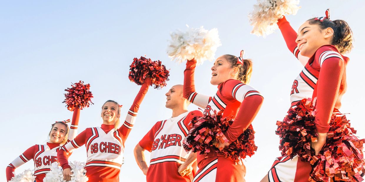 A group of cheerleaders in red uniforms cheering with pom-poms under clear sky.
