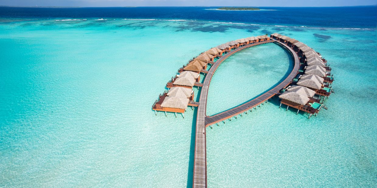 Overwater bungalows on a curved pier in turquoise water.
