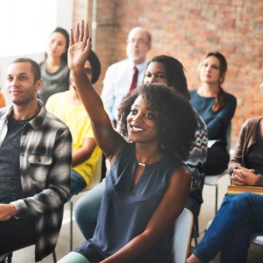 A smiling woman raises her hand in a diverse classroom setting.