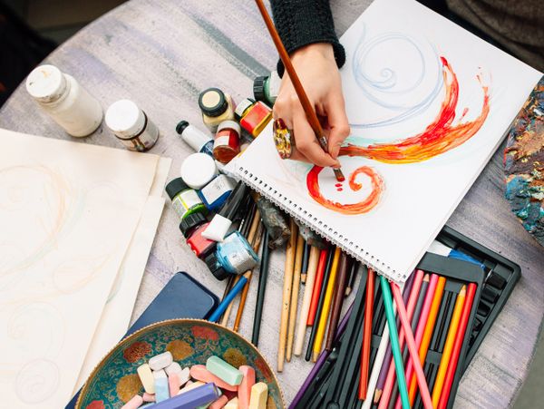 Person painting colorful swirls on paper with various art supplies around.