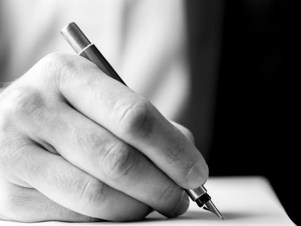 Close-up of a hand writing with a pen on paper.