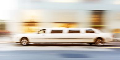 White limousine speeding down a city street with motion blur.