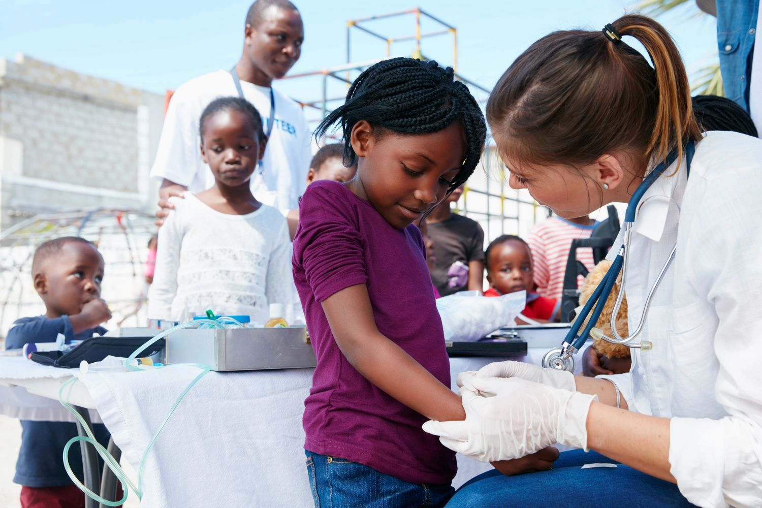 A healthcare worker examines a young girl's arm at an outdoor medical camp.