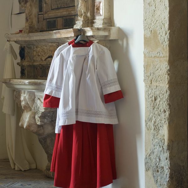 Religious vestments hanging on a wall near an ornate stone basin.