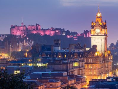 Edinburgh cityscape at dusk with illuminated castle and clock tower.