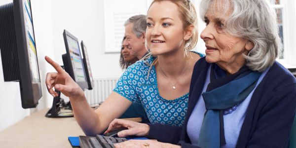 Young woman teaching elderly woman computer skills.