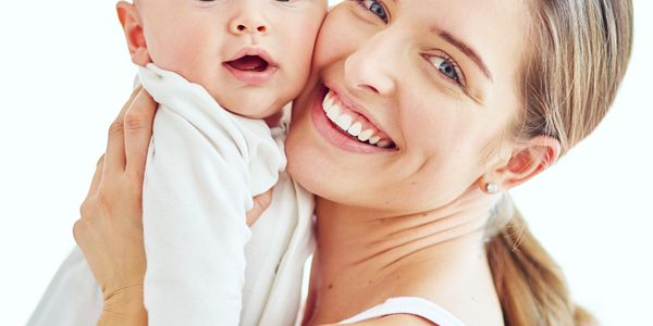 Mother smiling while holding her baby close, both looking at the camera.