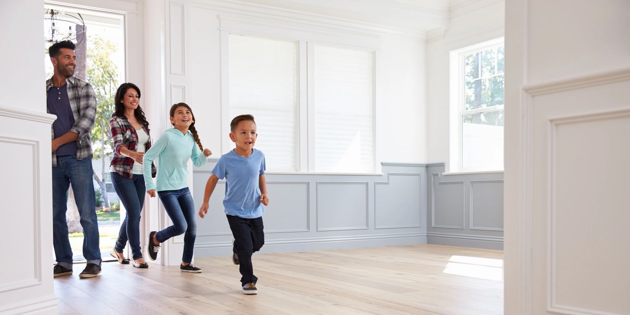 Happy family of four entering clean, empty house with son and daughter running through front door