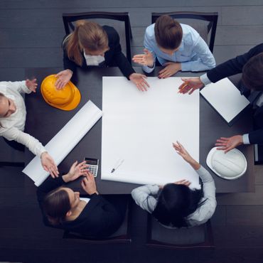 Top view of a team discussing architectural plans around a table with hard hats and tools.