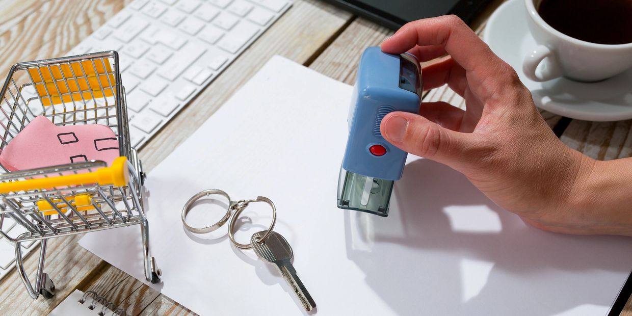 Hand stamping a document with a key and toy cart nearby.