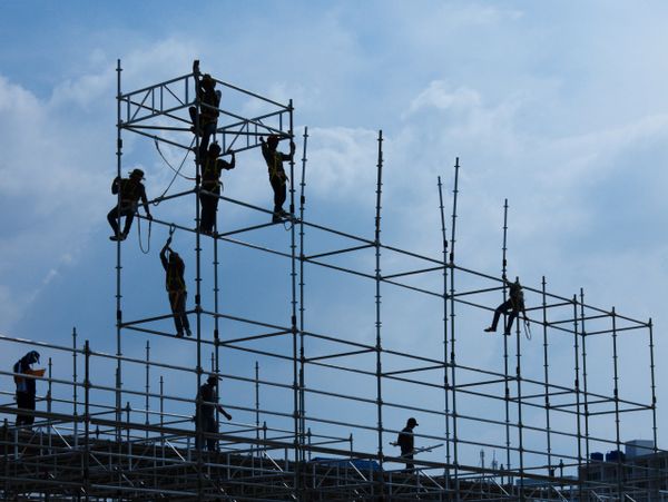 Workers assembling scaffolding against a blue sky.