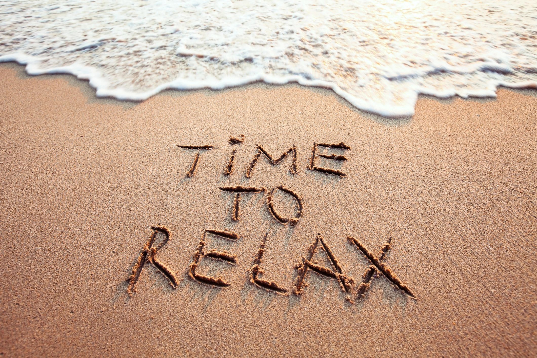 Words 'Time to Relax' written in sand near the ocean shore.