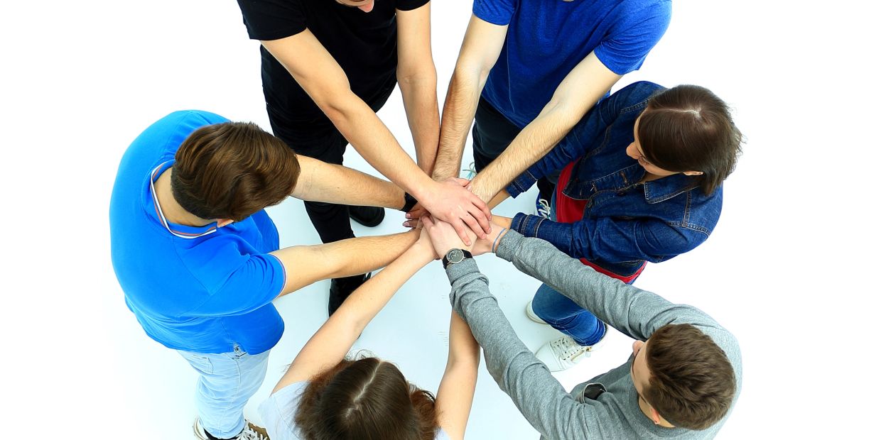 Group of young people joining hands in a teamwork gesture.