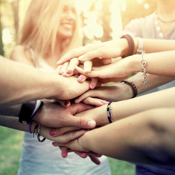 Group of friends stacking hands in a show of unity outdoors.