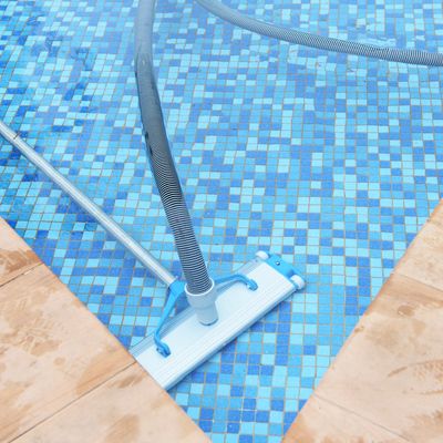 A pool vacuum cleaning the blue tiled floor of a swimming pool.