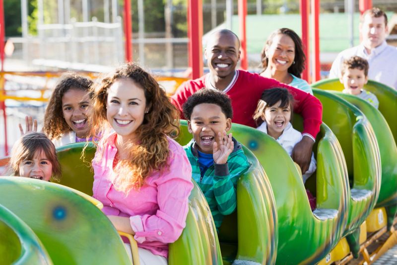Group of people on a rollercoaster ride at amusement park.  Focus on African American boy waving (6 years).